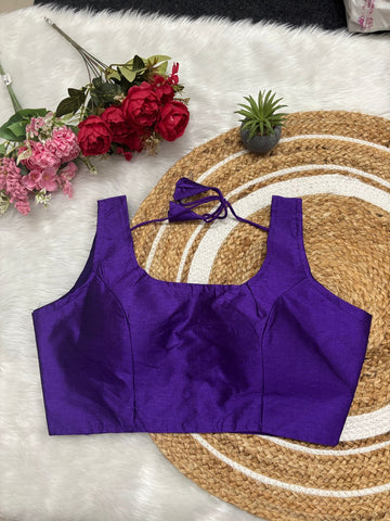 Purple top on a textured surface with flowers and a plant in the background