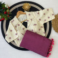 Beige blouse with floral patterns and a purple saree with pink tassels 