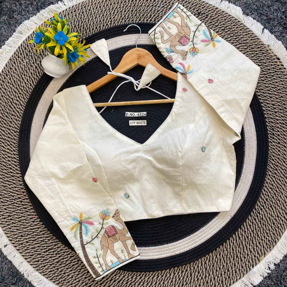 White embroidered blouse on a round mat with a hanger and decorative items.