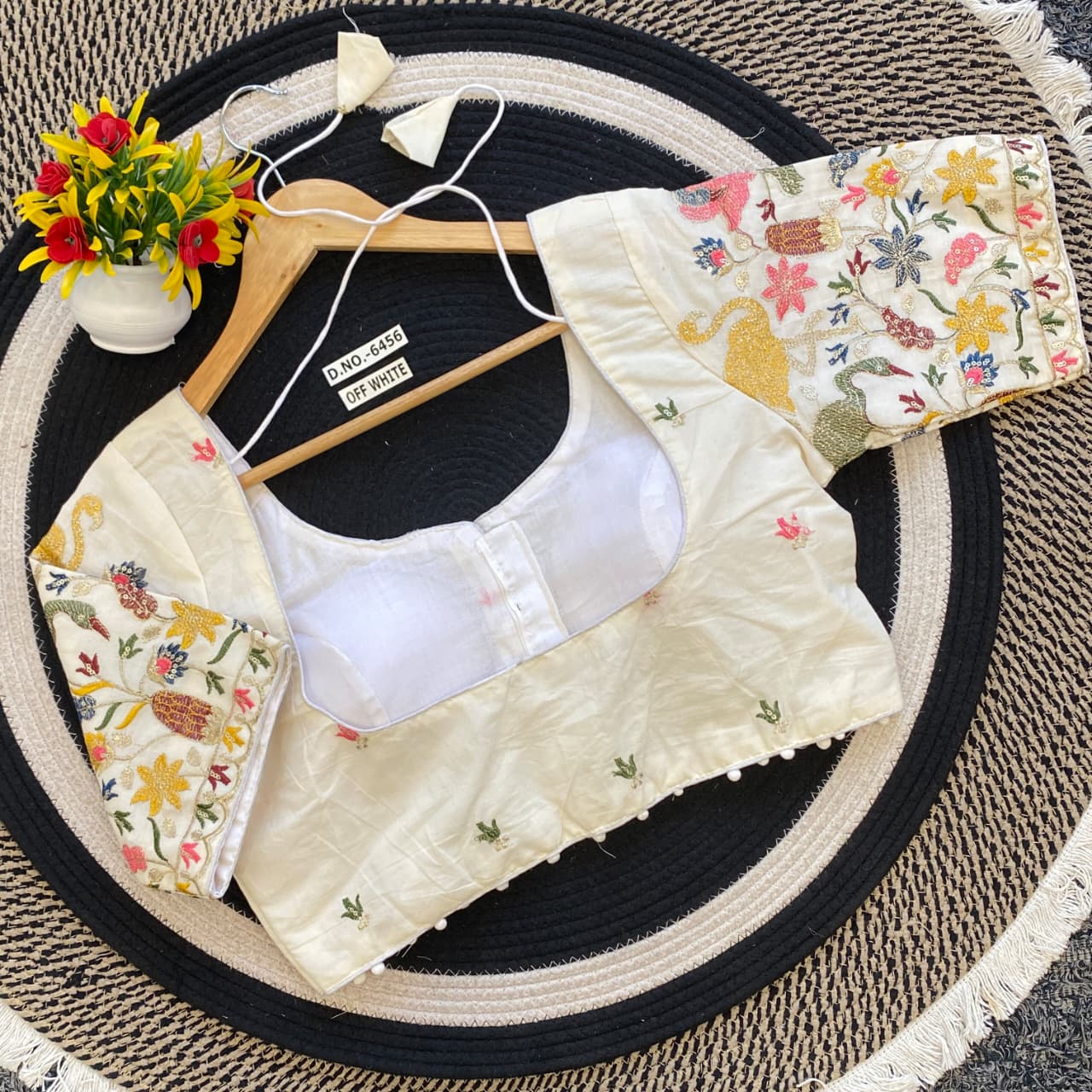 Embroidered blouse with floral collar and sleeves on a hanger against a textured surface.